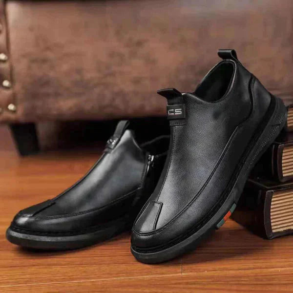 Black leather shoes on a wooden surface with a brown leather couch in the background