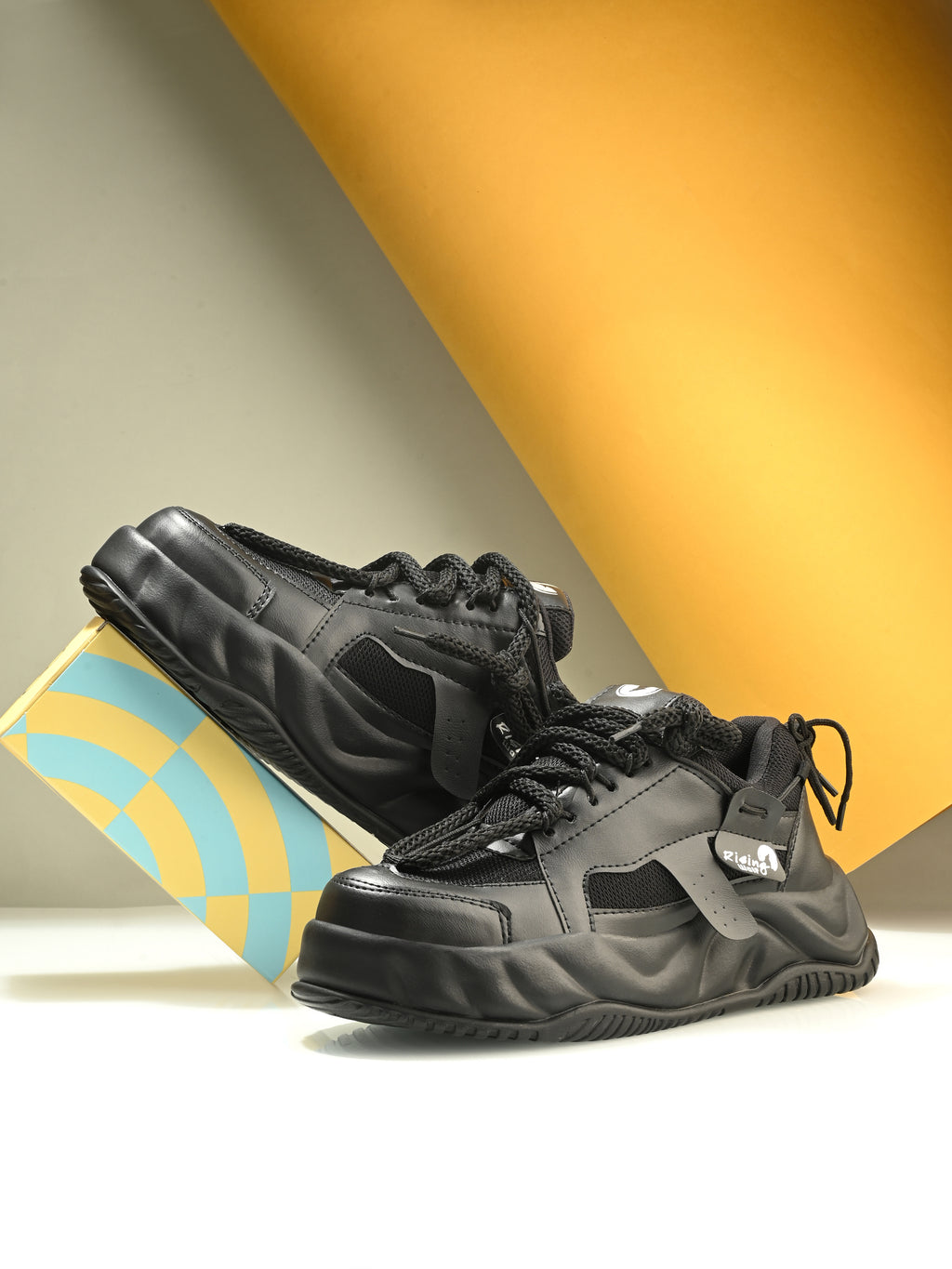 Black sneakers on a light surface with a colorful box in the background