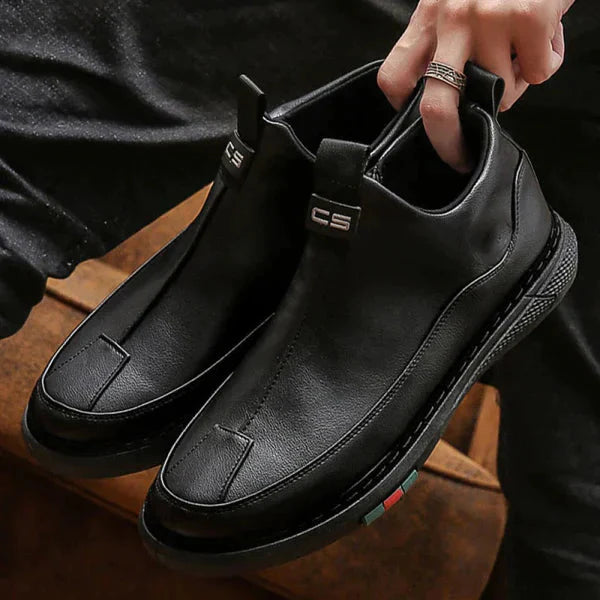 Black leather shoes held by a person against a dark background