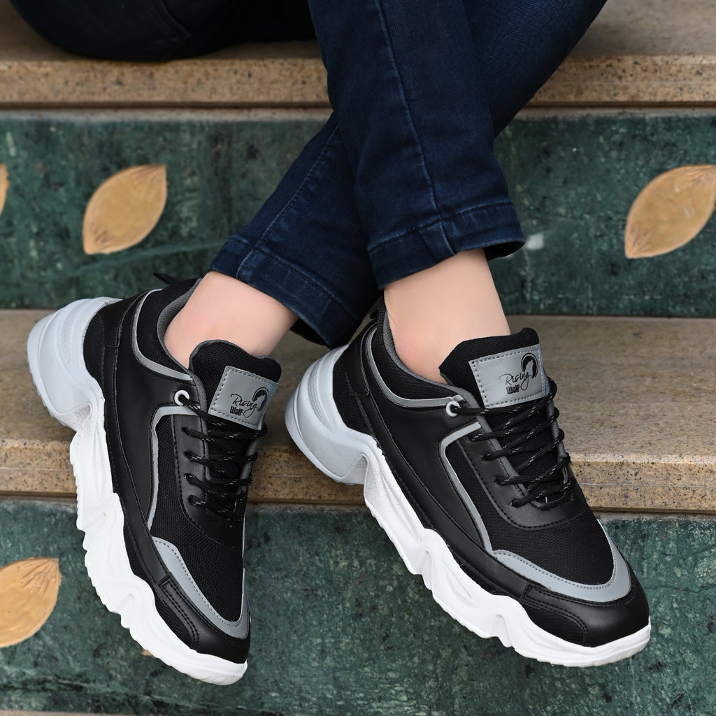 Black and gray sneakers with white soles worn by a person sitting on steps.
