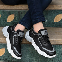 Black and gray sneakers with white soles worn by a person sitting on steps.