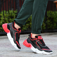 Black and red sneakers with white soles worn by a person on a blurred outdoor background