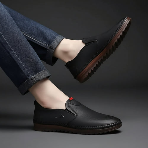 Black leather shoes worn with rolled-up jeans on a gray background