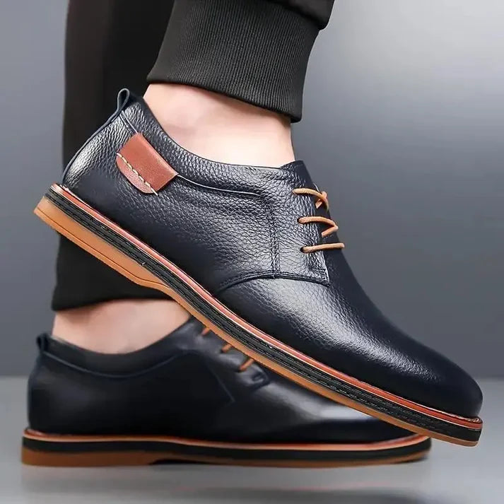 Black leather shoes with brown accents worn by a person on a gray background