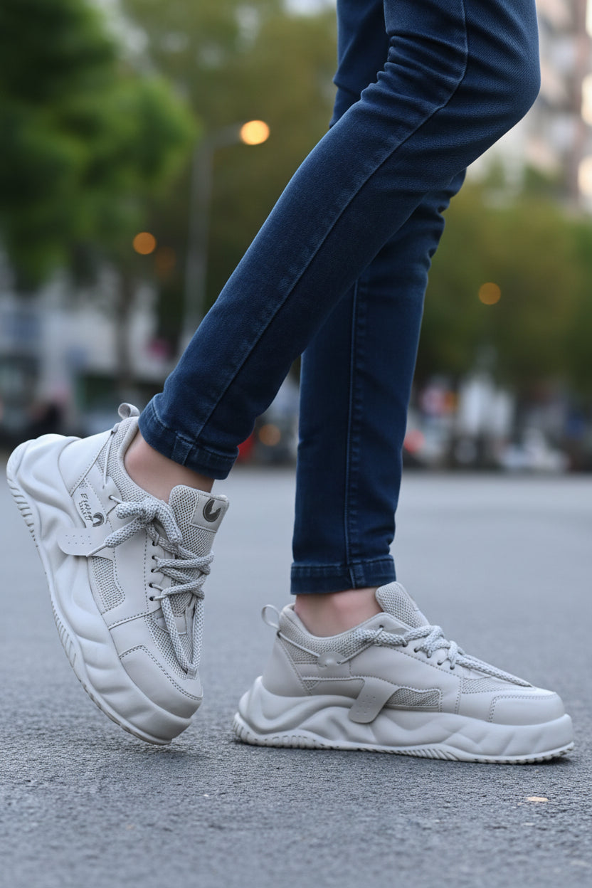 White sneakers worn with dark jeans on a road.