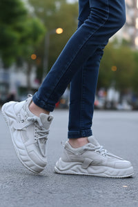 White sneakers worn with dark jeans on a road.